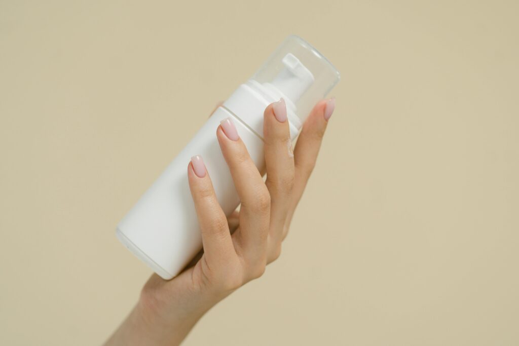 A close-up of a hand holding a white cosmetic bottle against a neutral background, perfect for product mockups and beauty industry use.